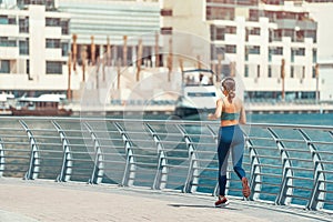 Rear view of sportive woman running and doing fitness exercises on the Dubai Marina embankment and listening to music with
