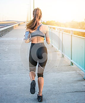 Rear view of sporty woman running over the bridge during sunny bright light.