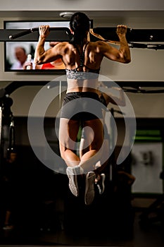 Rear view of strong muscular body of woman doing pull ups in gym.