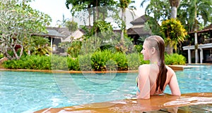 Rear view of a teenage girl leaning on the side of the pool. Luxury lifestyle people on vacation. Girl enjoying swimming