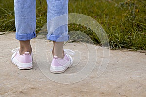 A rear view of a teenage girl& x27;s ankle in pink sneakers and blue jeans against a background of yellow dry grass. The