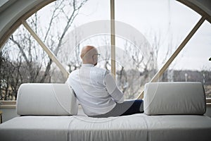 Rear view of thinking man relaxing on the sofa at home while looking out the window