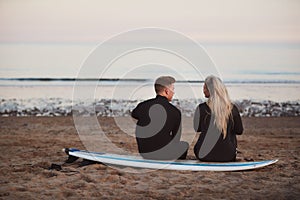 Rear View Of Thoughtful Couple Wearing Wetsuits On Surfing Staycation Looking Out To  Sea At Waves photo