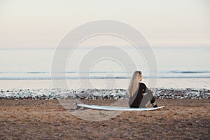 Rear View Of Thoughtful Woman Wearing Wetsuit On Surfing Staycation Looking Out To  Sea At Waves