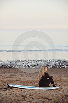 Rear View Of Thoughtful Woman Wearing Wetsuit On Surfing Staycation Looking Out To  Sea At Waves