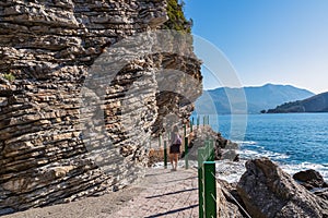 Rear view of touristic woman on Idyllic walk along steep high cliffs to the central beach Mogren of coastal tourist city of Budva