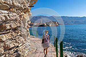 Rear view of touristic woman on Idyllic walk along steep high cliffs to the central beach Mogren of coastal tourist city of Budva