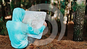 Rear view of traveler in blue hoodie holding the landmap while resting in pine forest