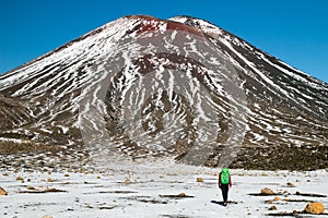 Rear view of the traveler and mountain tramper walking towards the Mount Ngauruhoe active volcano and caring the backpack