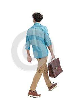 rear view of turkish man with curly hair holding suitcase and walking