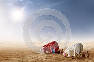 Rear view of two asian muslim man praying in prostration position on desert photo