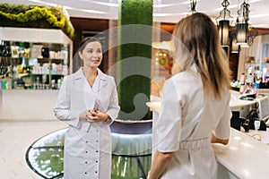 Rear view of two female doctors standing on hospital corridor discussing patient diagnose, looking to each other. Young