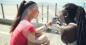 Rear view of two fit athletes using a phone after a workout training session in a sports stadium. Active, sporty young