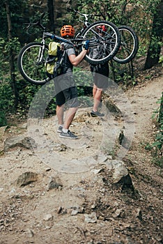 rear view of two male extreme cyclists in helmets carrying mountain bikes