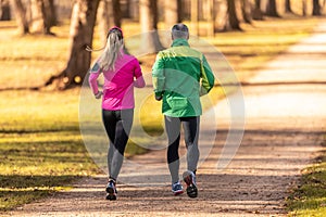 Rear view of a two runners, young woman and one mature man running in an autumn park