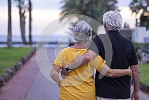 Rear view of two white-haired senior people walking happy enjoying their retirement and beach vacation. Serene and in love couple