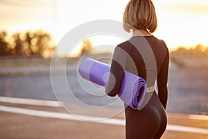 Rear view on unrecognizable fit female holding mat for sport exercises