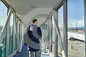 Rear view of unrecognizable male traveller walking along airport with backpack. Back view of man passing terminal gate