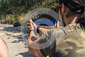 Rear view of white man in camo t-shirt practising how to aim handgun. Firearm training at firing range. Outdoor