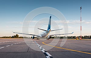 Rear view of wite \'n\' blue modern widebody passenger airplane on airport apron at sunset.