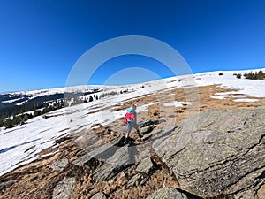 Rear view of woman with backpack hiking on snow covered alpine meadow to Steinerne Hochzeit, Saualpe, Lavanttal Alps photo