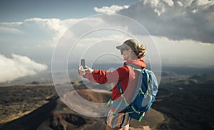 Rear view of woman backpacker taking photo with smart phone