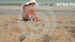 Rear view of woman in a bikini and sun hat while sunbathing on sea sand paradise beach