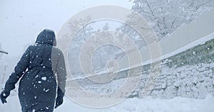 rear view of a woman in a black coat walking through a snow storm in the countryside
