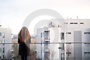 Rear view of woman with curly hair standing on terrace, enjoying cold autumn morning, sunny day. Speaking positive