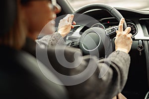 Rear view of woman driving car and holding both hands on steering wheel on the way to work