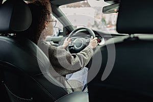 Rear view of woman driving car and holding both hands on steering wheel on the way to work