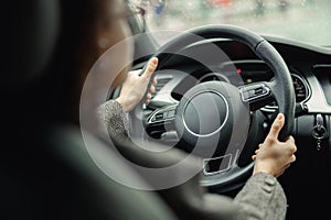 Rear view of woman driving car and holding both hands on steering wheel on the way to work