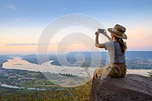 Rear view of woman enjoys Mekong river high angle view photographing by smart phone on the cliff