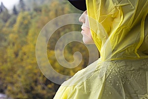 Rear view woman hiker in yellow raincoat hide from rain in forest