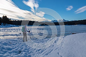 Rear view of woman with hiking backpack watching the frozen lake Forstsee, Techelsberg, Carinthia (Kaernten), Austria,