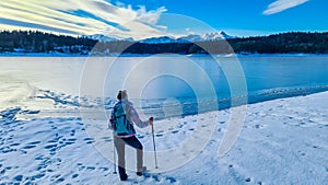 Rear view of woman with hiking backpack watching the frozen lake Forstsee, Techelsberg, Carinthia (Kaernten), Austria,