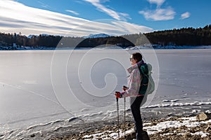 Rear view of woman with hiking backpack watching the frozen lake Forstsee, Techelsberg, Carinthia (Kaernten), Austria,