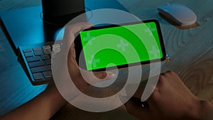 Rear view of woman holding Chroma Key green screen of smartphone in horizontal position. She scrolls through content by