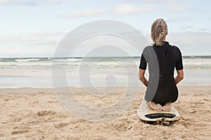 Rear view of woman kneeling on surfboard against cloudy sky