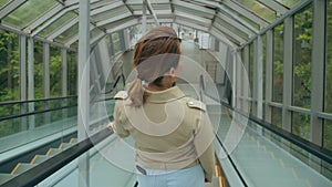 Rear view, woman in leather jacket and blue jeans on an escalator in a transparent tunnel