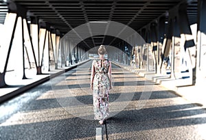 rear view of a woman in long dress walking in the middle of a road under bridge