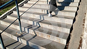 Rear view of a woman in a long gray dress and white sneakers walking down the sidewalk and up the stairs.