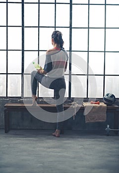 Rear view of woman looking out window holding water in loft gym