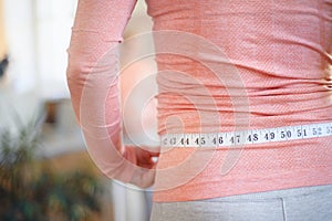 Rear view of woman measuring her pregnant belly in front of a mirror.