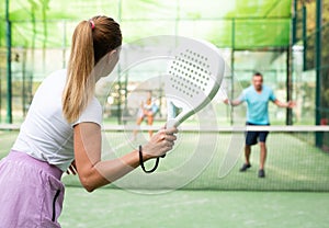 Rear view of woman playing paddle tennis match on outdoor court on blurred background of opponents