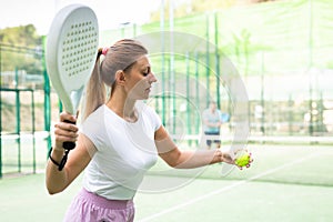 Rear view of woman playing paddle tennis match on outdoor court on blurred background of opponents