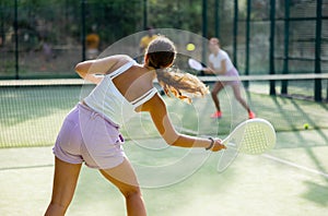 Rear view of woman playing paddle tennis match on outdoor court on blurred background of opponents