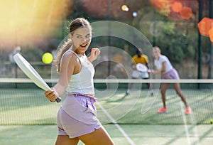 Rear view of woman playing paddle tennis match on outdoor court on blurred background of opponents