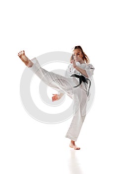 Rear view. Woman professional karate fighter with black belt performing kick in action isolated over white background.