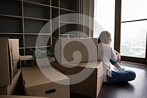 Rear view woman sit alone on floor near cardboard boxes